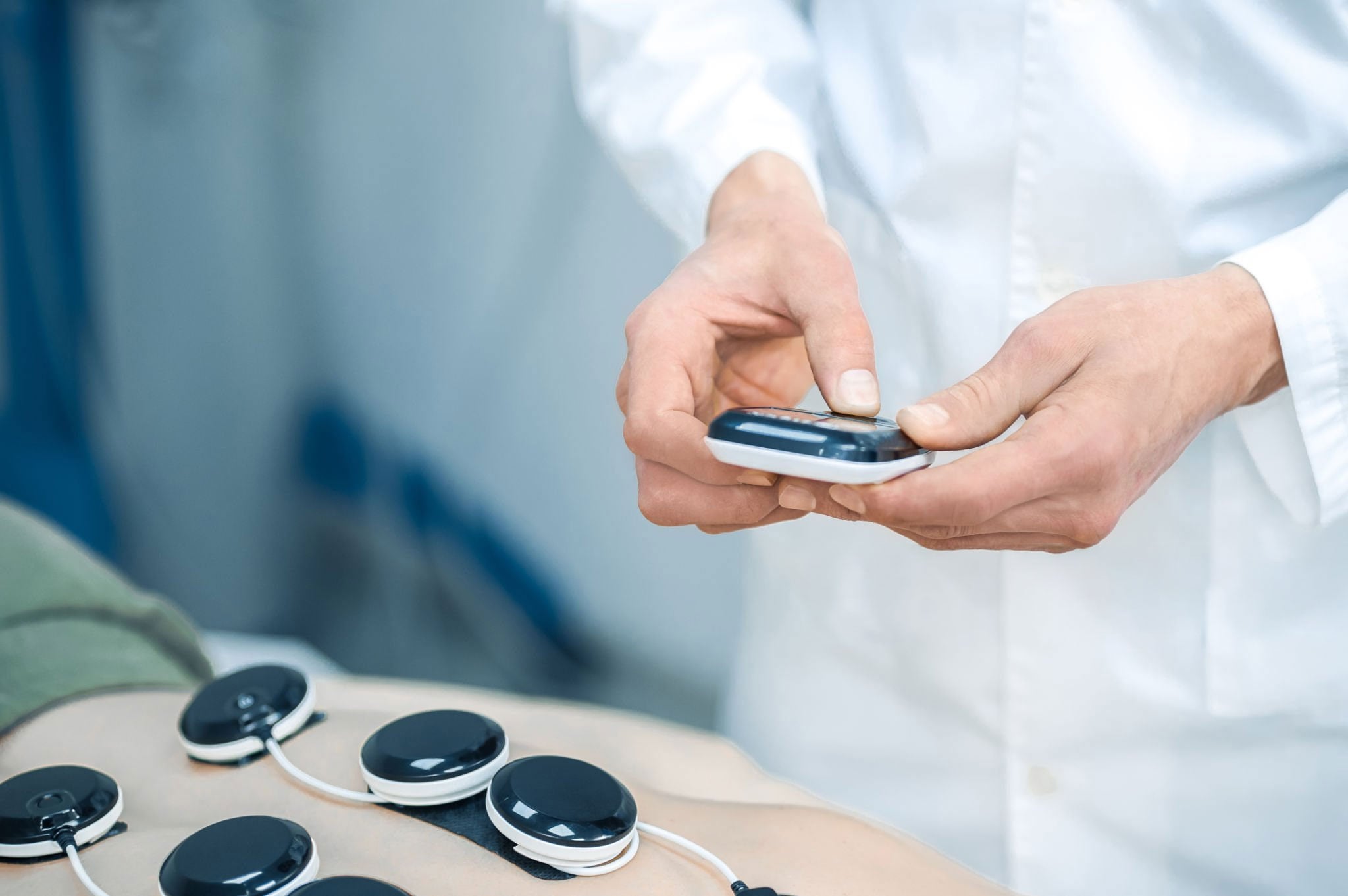 Clinician in a white coat holding a device above circular pads on a patient's skin